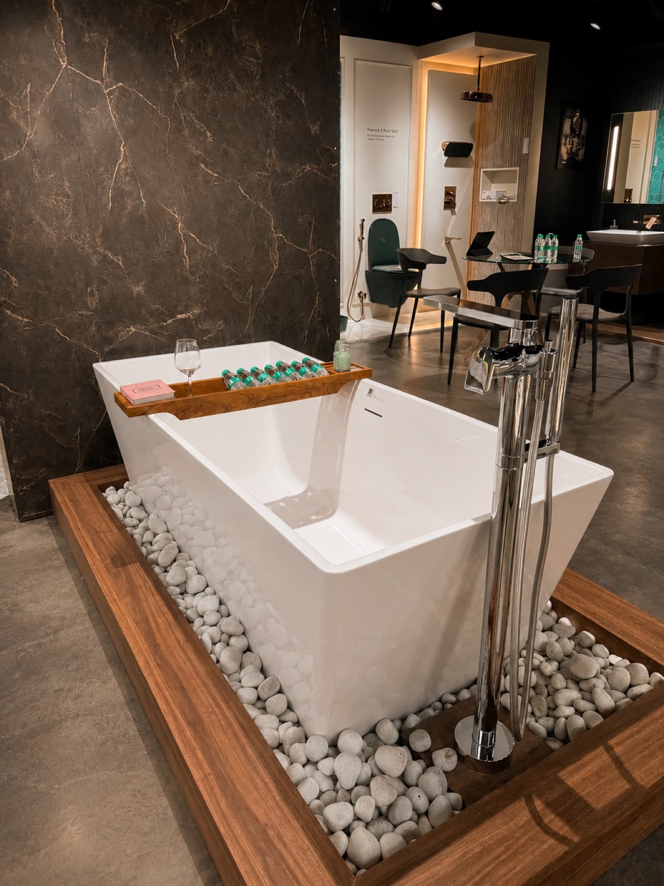 Freestanding Kohler bathtub with floor-mounted chrome filler on a pebble plinth at Tayo Living, Gurgaon