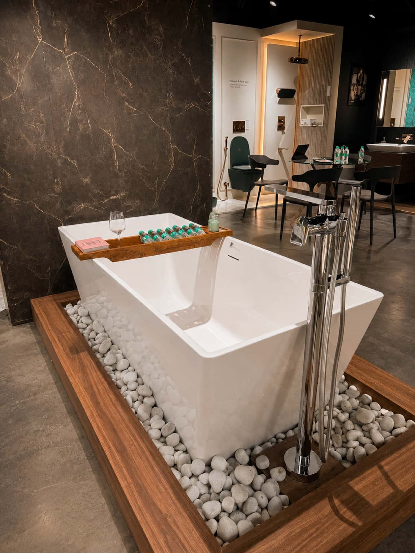 Freestanding Kohler bathtub with floor-mounted chrome filler on a pebble plinth at Tayo Living, Gurgaon